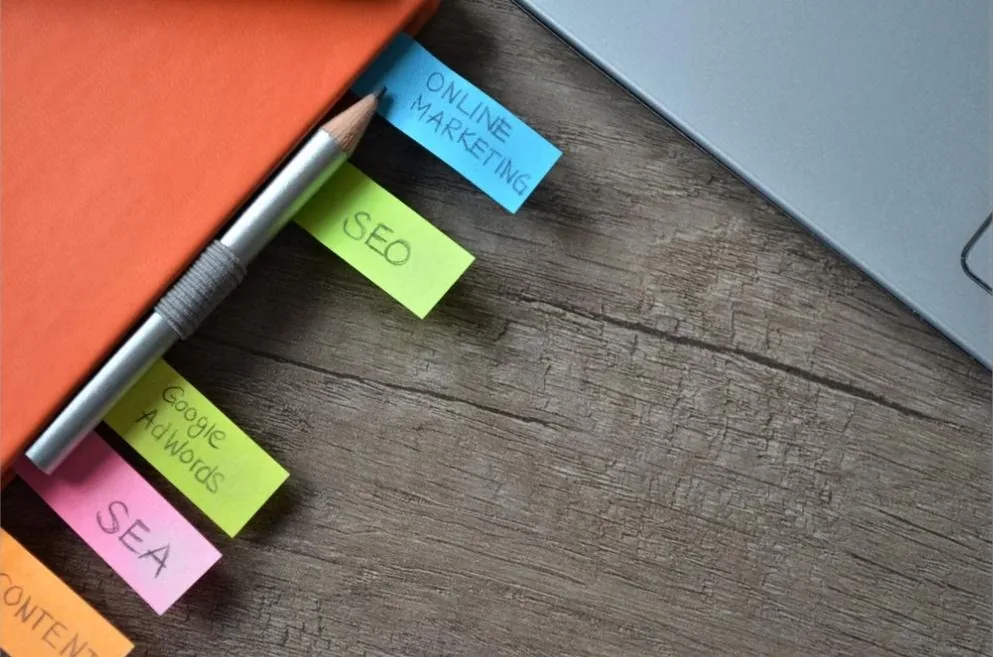 Sticky notes labeled SEO, SEA, Google AdWords, and Online Marketing on a desk next to a laptop, representing entity relationships in AEO content