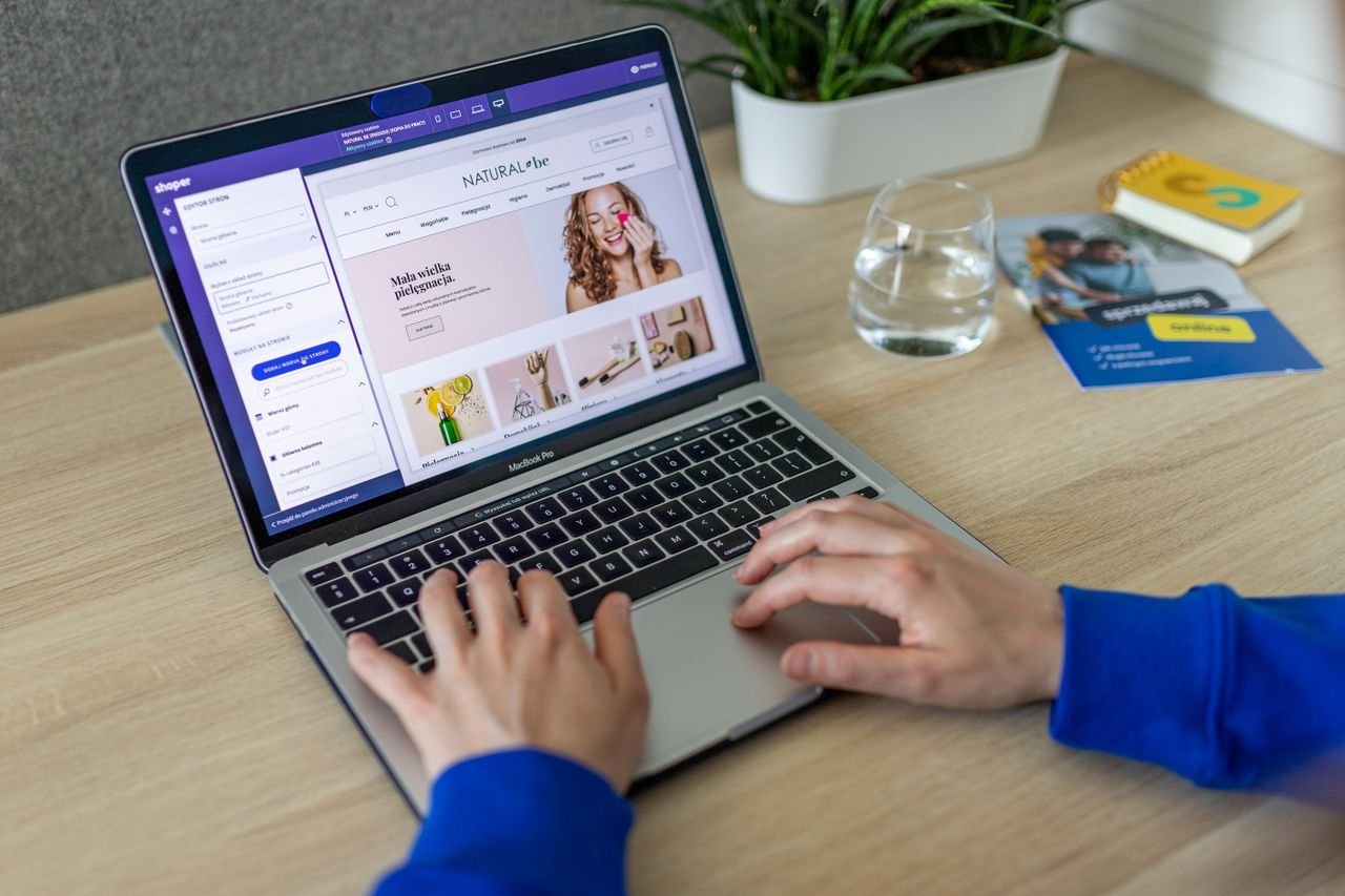 Home Hands typing on a laptop showing an e-commerce website in a modern office setting.