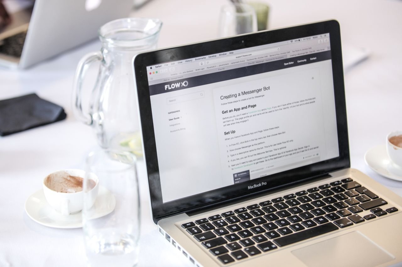 Home Close-up of a MacBook Pro displaying a webpage, with coffee cups and water pitcher on a table.