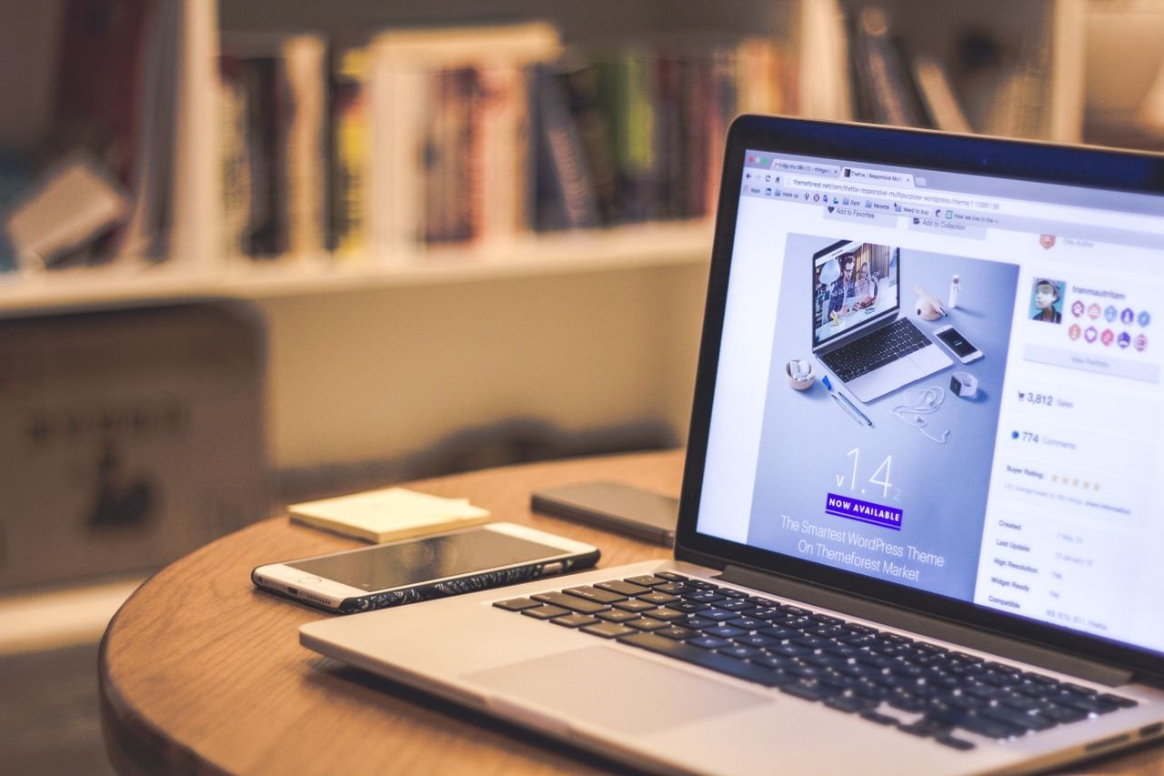 Home A cozy modern workspace featuring a laptop displaying a website, a smartphone, and books on shelves.